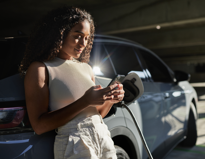 A woman leans against her car with a mobile phone in her hand