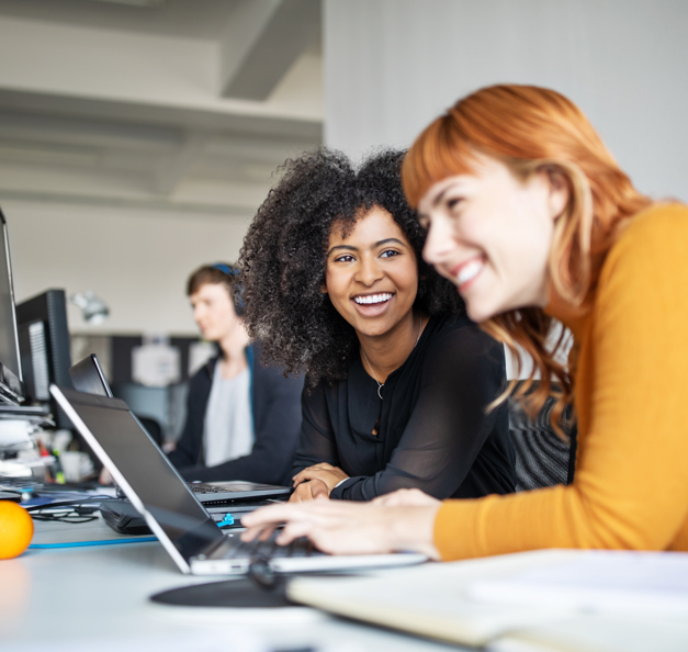 two young women in front of their laptops smiling 