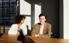 Mann im hellbraunen Sakko, gemeinsam mit einer Frau an einem Tisch sitzend.