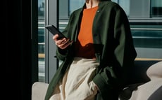 Frau in dunkelgrünem Mantel und rotem Pullover mit einem Smartphone in der Hand.
