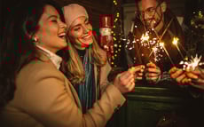 Eine Freundesgruppe steht draußen und feiert mit Sekt und Wunderkerzen in das neue Jahr