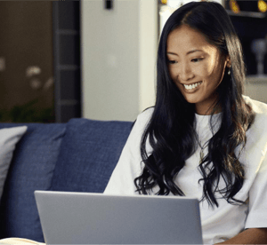 Smiling woman sitting on a couch, using a laptop for online shopping and paying in three.