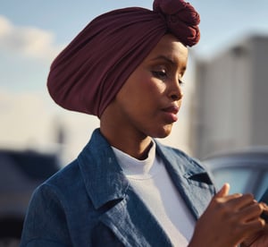 Focused woman wearing a headscarf, standing outdoors and using her smartphone for digital payments.