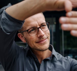 A man wearing glasses raises his hand, signaling in a focused setting.
