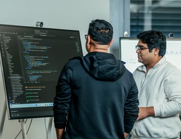 Zwei Entwickler, die vor einem Monitor stehen, auf dem Code zu sehen ist.