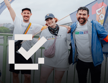 Checklist item marked as complete. Three employees smiling and posing together at a Pride event while holding flags and wearing company-branded clothing. The image highlights community engagement, inclusion, and support for diversity in the workplace.