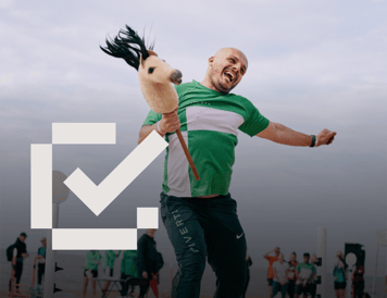 Checklist item marked as complete. Employee in a green and white sports shirt laughing while running with a hobby horse during an outdoor company event. Other participants and spectators can be seen in the background, highlighting a fun and inclusive workplace culture.