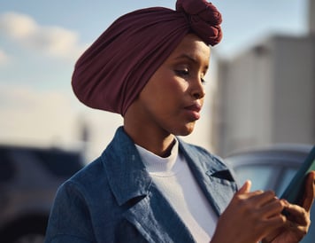 Fokusert kvinne med hodeskjerf står utendørs og bruker smarttelefonen sin for digitale betalinger.