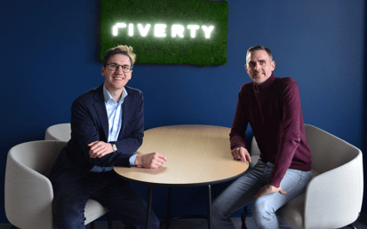 Vertreter von Riverty und Sinpex lächeln mit einem Riverty-Logo hinter sich