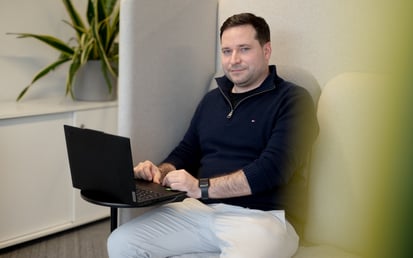 Mann sitzt in einem gepolsterten Bürositz und arbeitet am Laptop.