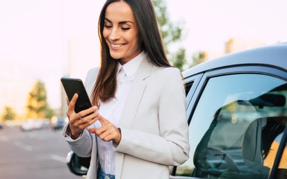 Woman standing at a parking lot next to car smiling down at her phone