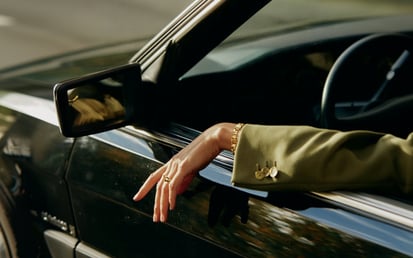 Hand einer Frau, die ihre Hand aus einem grünen Auto hält und einen grünen Anzug trägt.