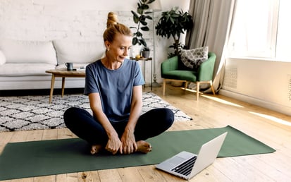 Frau mit Laptop, die auf einer Yogamatte sitzt.