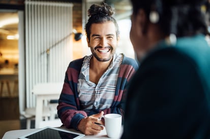 a man with a cup of coffee smiling into the camera