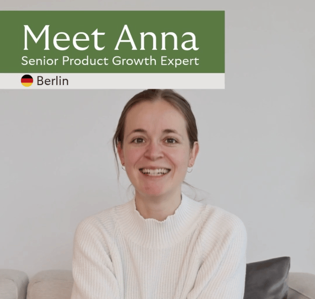 A portrait photo shows a smiling person centered in the frame, sitting on a light-colored sofa in front of a plain, light wall. The person wears a light knitted sweater and has hair pulled back. A dark cushion is visible on the right side of the sofa. At the top, a wide green banner contains white text: “Meet Anna”. Below it reads “Senior Product Growth Expert”. On the left there is a small German flag icon followed by “Berlin”. The image is presented like a team/profile introduction (the person is introduced as an expert)