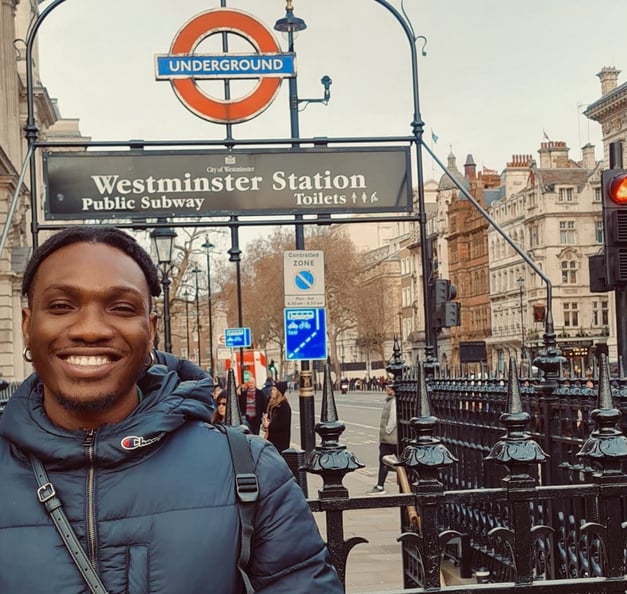 Timothy warmly dressed, standing in front of a 'Westminster Station' sign