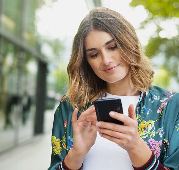 Ung, leende kvinna på stan med en smartphone i handen.