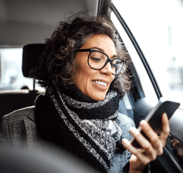 Frau sitzt im Auto und schaut auf ihr Handy