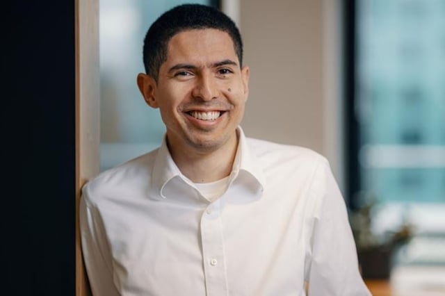 Smiling man wearing a white shirt, standing indoors in an office environment
