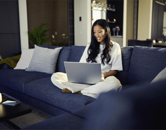 Afbeelding van een vrouw die met haar laptop bezig is en op de bank zit.