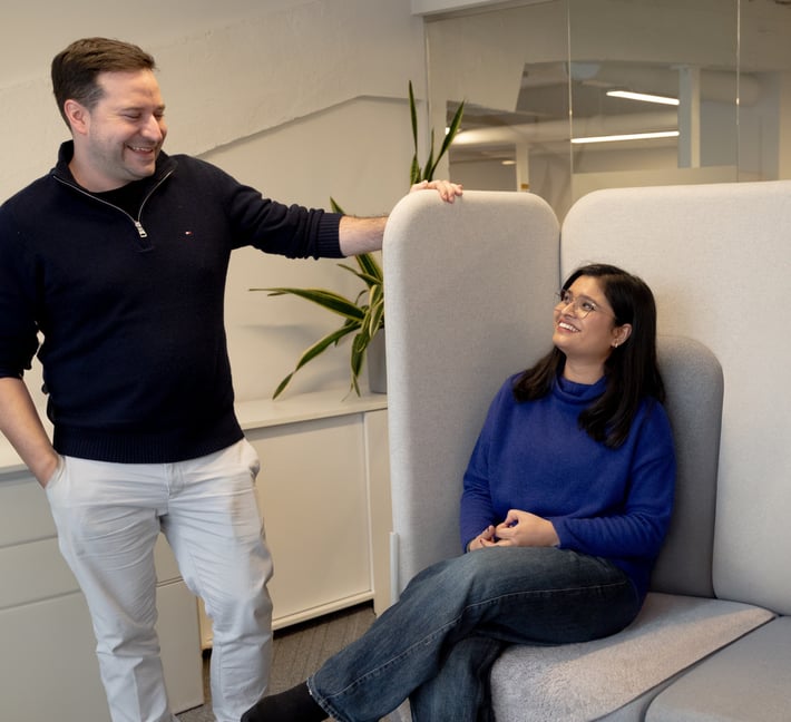 Two coworkers smiling and chatting in a modern office seating area.
