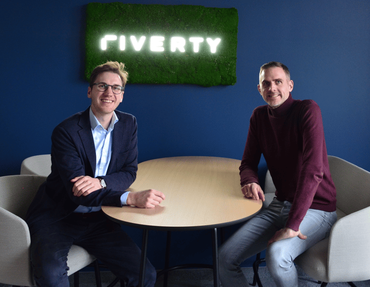 Vertreter von Riverty und Sinpex lächeln mit einem Riverty-Logo hinter sich