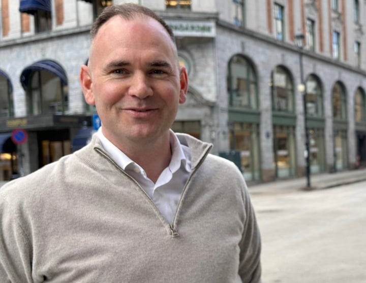 Portrett av en mann som står i en bygategate med historiske forretningsbygg i bakgrunnen