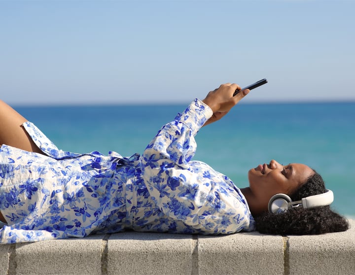 En vrouw ligt met een koptelefoon en een telefoon in haar hand
