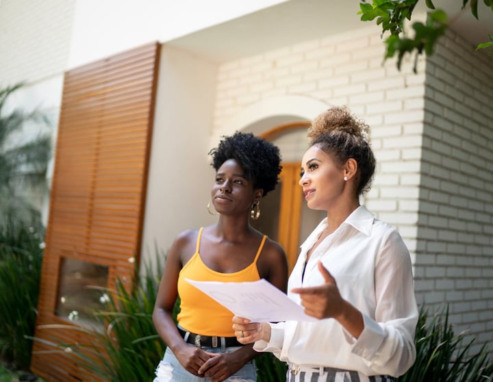 Eine brünette Frau und eine blonde Immobilienmaklerin schauen sich gemeinsam eine Immobilie an und sprechen über die Investitionsmöglichkeiten