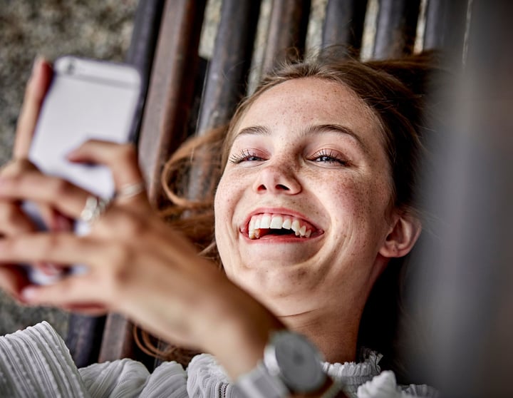 Lachende vrouw beheert haar financiën met Riverty Back in Flow op haar telefoon