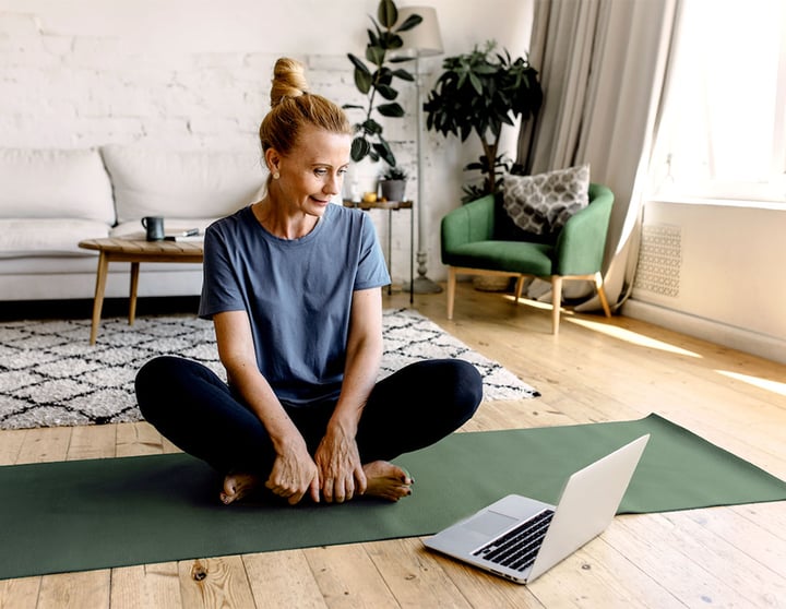 Frau mit Laptop, die auf einer Yogamatte sitzt.